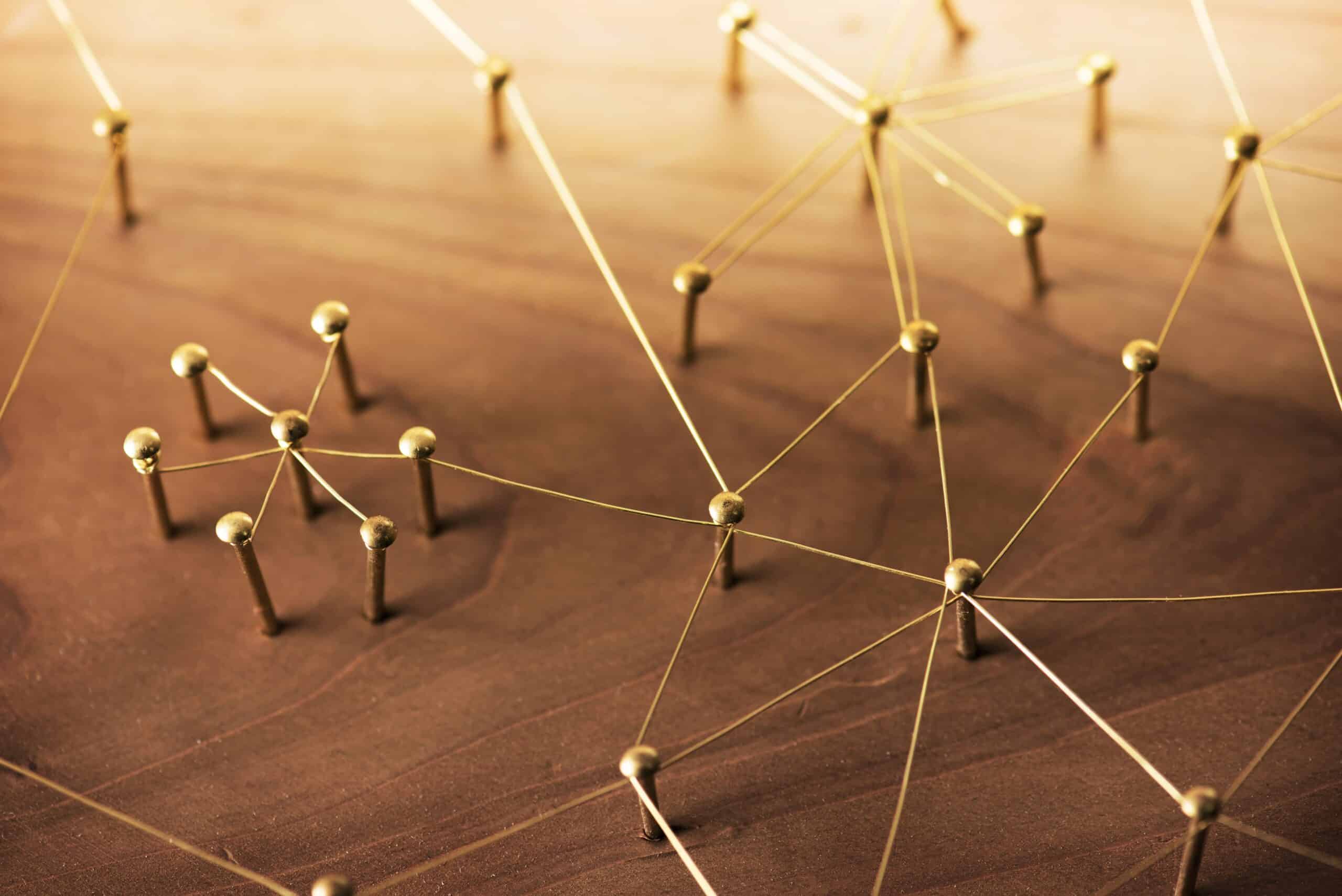 Multiple brass pins linked with golden strings creating a web of connections on a wooden surface.